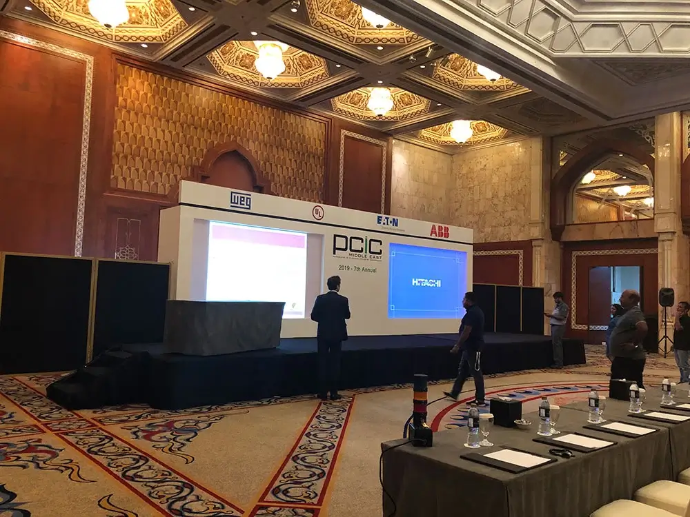 Conference stage backdrop featuring company logos at an event, with a speaker presenting.